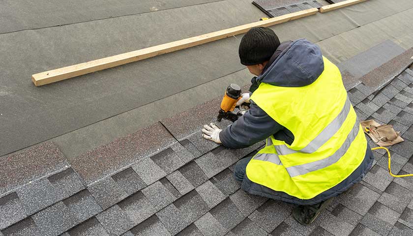 Workman using pneumatic nail gun install tile on roof